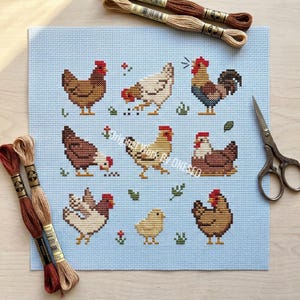 May include: A cross-stitch pattern featuring various chickens and a chick on a light blue background. The chickens are in shades of brown, white, and tan, with red combs. Embroidery floss and scissors are also visible. The artwork is a handmade craft project.
