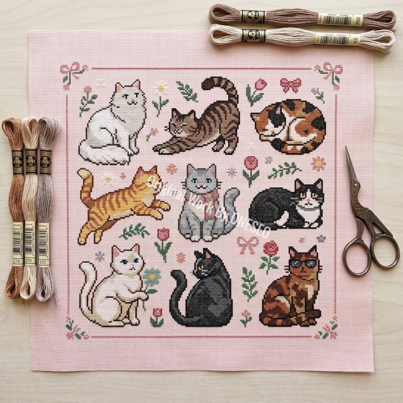 May include: A pink needlepoint canvas featuring nine different cat designs in various poses and colors, surrounded by floral and bow motifs. Embroidery floss and scissors are also visible.