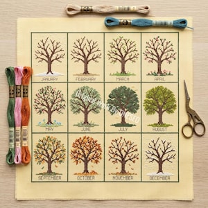 May include: Cross-stitch project featuring a seasonal tree design. The canvas displays twelve trees, each representing a month. Embroidery floss in green, pink, and beige, along with scissors, are also visible.