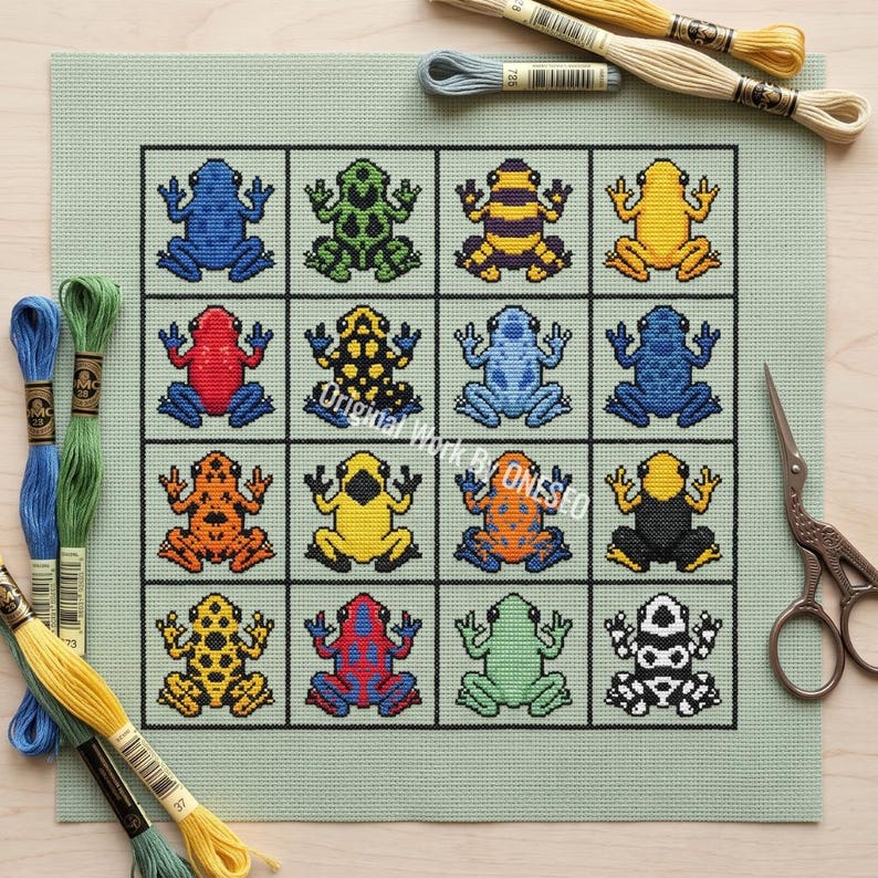 May include: A light green cross-stitch fabric featuring a grid of sixteen colorful poison dart frogs in various patterns and colors, including blue, red, yellow, orange, green, and black. Embroidery floss skeins and metal scissors are included.