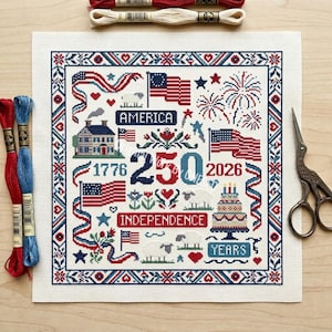 May include: A cross-stitch design featuring patriotic symbols in red, white, and blue. The design includes American flags, fireworks, a house, sheep, and the text "America," "Independence," "1776," "250," "2026," and "Years."