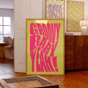 May include: A framed poster with the words "GROOVY BABY YEAH!" in bright pink against a yellow-green background. Two additional framed posters are visible, one with the word "DISCO" and another with a checkered pattern.