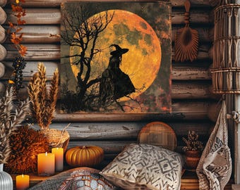May include: A square wall art print featuring a silhouette of a witch sitting on a bare tree branch against a large, glowing orange full moon. The artwork is displayed in a rustic setting with candles, pumpkins, and patterned throw pillows.