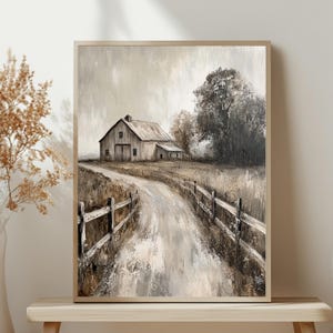 May include: A framed wall art print featuring a neutral-toned landscape painting of a rustic barn situated at the end of a dirt path. The scene includes a wooden fence lining the road, tall dry grasses, and a large tree under a cloudy sky.