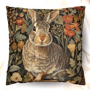 May include: A square throw pillow featuring a detailed illustration of a brown rabbit centered against a dark background filled with orange, yellow, and green botanical elements including various flowers, leaves, and stems in a dense pattern.