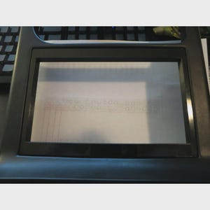 Op de afbeelding: Een zwart kunststof dashboardpaneel voor een autoradio met een rechthoekige opening in het midden. Het frame heeft een gladde, matte afwerking en is ontworpen voor een infotainmentscherm, met een doorzichtige beschermfolie over het midden.