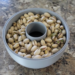 May include: A gray ceramic bowl filled with shelled pistachios. The bowl has a center ring that is also gray.