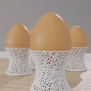 Puede incluir: Tres huevos marrones en soportes para huevos de encaje blanco. Los soportes están hechos de un diseño delicado y calado.