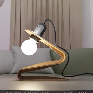 May include: A wooden lamp with a unique design, featuring a curved base and a light bulb. The lamp is on a table with a green sofa in the background. The text "DIGITAL DOWNLOAD .DXF .SVG" is visible at the bottom of the image.