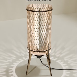 May include: A wooden lamp with a geometric pattern and a black cord. The lamp is on a white surface and casts a shadow on the floor.