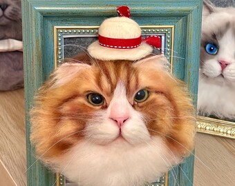 May include: A framed needle felted portrait of a cat wearing a white and red hat. The cat has orange and white fur and is looking directly at the viewer. The frame is teal green with gold accents.