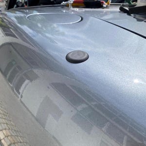 Könnte beinhalten: Nahaufnahme eines silbernen Autos mit einer schwarzen Antennenkappe. Das Auto hat eine schwarze Gummidichtung um die Heckscheibe und ein rotes Rücklicht.
