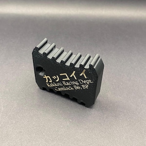 Könnte beinhalten: Ein schwarzer Kunststoff-Camlock-Schlüssel mit dem Text "Kakkou Racing Dept. Camlock Bo, BP" und dem japanischen Text "カッコーイ" in goldener Schrift.