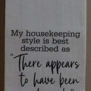 May include: White kitchen towel with black text that reads "My housekeeping style is best described as "There appears to have been a struggle."