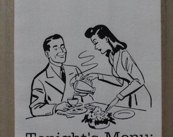 May include: White kitchen towel with a black and white illustration of a couple at a table. The text "Tonight's Menu: Eat it or Starve" is printed below the illustration. The towel is hanging on a wooden rod.
