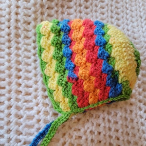 May include: A colorful crocheted baby hat with a rainbow pattern and a long green and blue tie.