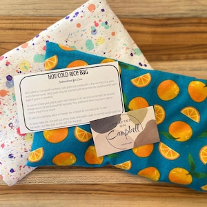 Könnte beinhalten: Ein Heiß- und Kalt-Reissack mit einem blauen und orangefarbenen Citrus-Druckstoffbezug. Der Beutel ist mit einem flanellgefütterten Reissack ausgestattet und duftet. Eine Anleitung zur Verwendung ist auf einer weißen Karte enthalten.