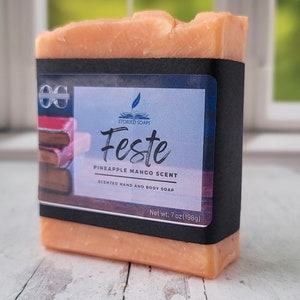 Può includere: Un sapone con un'etichetta nera che recita "STORIED SOAPS Feste PINEAPPLE MANGO SCENT SCENTED HAND AND BODY SOAP Net wt. 7 oz (198g)".