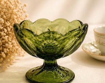 May include: A green glass dessert bowl with a pedestal base. The bowl has a scalloped rim and a floral design. The bowl is approximately 5 inches in diameter and 4 inches tall. The bowl is sitting on a white surface.