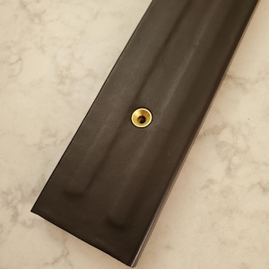 May include: A dark brown leather strap with a gold metal grommet.