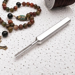 May include: A silver metal tool for threading beads, a brown spool of thread, and a multi-colored beaded rosary with a black cross.