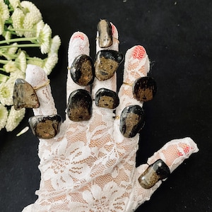 May include: A hand wearing a white lace glove with multiple rings on each finger. The rings are made of black stone with gold bands.