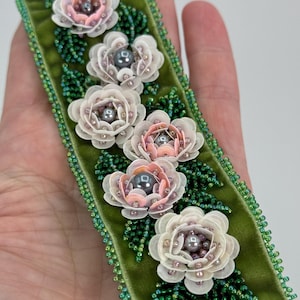 May include: A green velvet bracelet with white and pink flower embellishments. Each flower is made of sequins and has a pearl in the center.