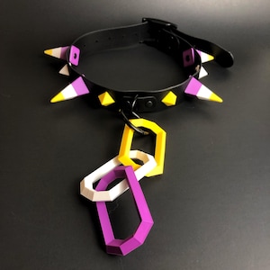 May include: A black leather collar with yellow and purple spikes and a chain with three linked rings in yellow, white, and purple.