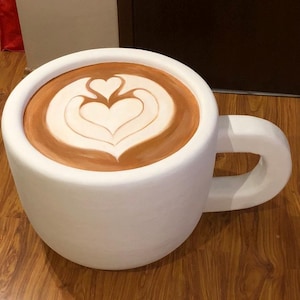 Puede incluir: Una taza de café grande de cerámica blanca con café marrón y un diseño de arte latte en forma de corazón blanco.