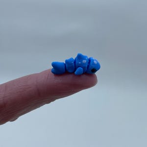 May include: A small blue and white figurine of a segmented worm with black eyes. The worm is curled up and appears to be made of polymer clay.