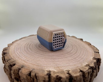 May include: A small, beige and blue plastic pet carrier with a wire door. The carrier is sitting on a wooden surface.