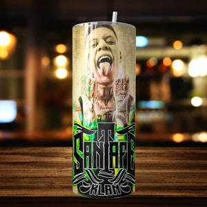 May include: A stainless steel tumbler with a green, black, and white design featuring a portrait of a man with tattoos and the text "The Santa Fe Klan".