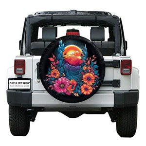 May include: A black spare tire cover with a colorful floral design and a sunset scene. The tire cover features a mountain range, cacti, and a full moon. The text "STYLE MY WHIP TIRE COVERS & MORE" is printed on the bottom left corner of the cover.