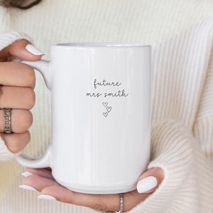 Pu&ograve; includere: Tazza in ceramica bianca con testo nero che recita "future mrs. smith" con tre piccoli cuori sotto il testo.