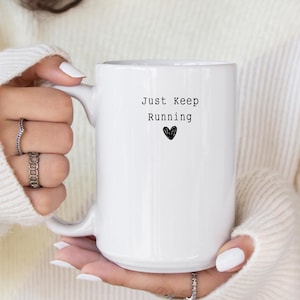 May include: White ceramic mug with a black inscription that reads "Just Keep Running" with a small black heart below the text.