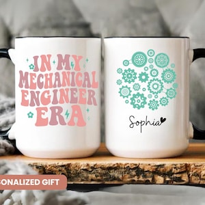 May include: Two white ceramic mugs with black handles and rims. One mug features the text "IN MY MECHANICAL ENGINEER ERA" in pink and peach. The other mug has a gear design and the name "Sophia".