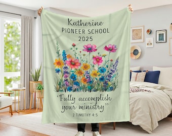 May include: A light green blanket featuring a watercolor floral design with colorful flowers. The blanket has text that reads "Katherine PIONEER SCHOOL 2025" and "Fully accomplish your ministry" with a Bible verse reference.