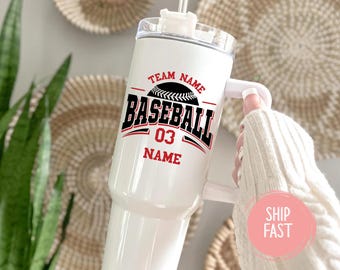May include: White baseball tumbler with a black and red design. The tumbler features the words "Team Name" above a baseball graphic, with "BASEBALL" and "03" in bold lettering. The word "NAME" is below. A white handle is attached.