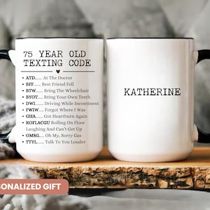 May include: White ceramic mug with a black handle and rim. The mug features the text "75 YEAR OLD TEXTING CODE" and a list of abbreviations with their meanings. The name "KATHERINE" is printed on the other side. The mug is a personalized gift.