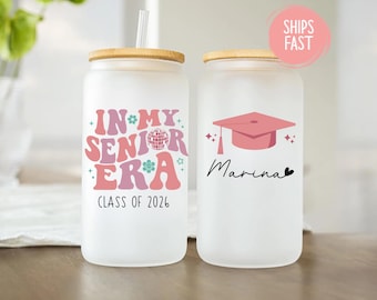 May include: Two frosted glass tumblers with bamboo lids. One features the text "IN MY SENIOR ERA CLASS OF 2026" in pink and purple. The other has a pink graduation cap and the name "Marina".