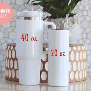 May include: Two white insulated tumblers with straws, one labeled "40 oz." and the other "20 oz." in red text. The tumblers are on a light-colored surface, with a decorative background and a plant in a white pot.