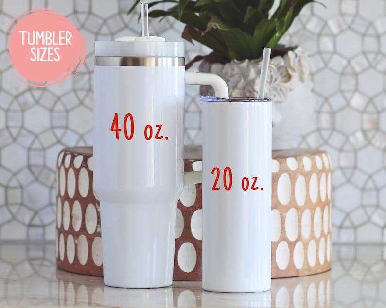 May include: Two white insulated tumblers with straws, one labeled "40 oz." and the other "20 oz." in red text. The tumblers are on a light-colored surface, with a decorative background and a plant in a white pot.