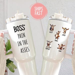 May include: Two white insulated tumblers with handles. One tumbler has the text "BOSS' PAIN IN THE ASSES" in black. The other tumbler features cartoon donkey illustrations with names: Alex, Emily, Mark, Samuel, and Karl.