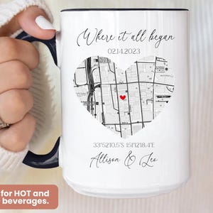 May include: White ceramic mug with a black rim and handle. The mug features a black and white map of a city in the shape of a heart with a red dot in the center. The text "Where it all began" is printed above the map, followed by the date "02.14.2023". Below the map, the coordinates "33&deg;52'10.5'S 151&deg;12'18.4'E" and the names "Allison & Lee" are printed.