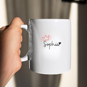 May include: White ceramic mug with a pink crown and the name "Sophia" written in black cursive with a small black heart.