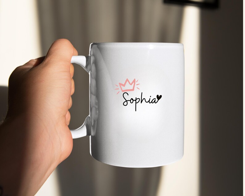 May include: White ceramic mug with a pink crown and the name "Sophia" written in black cursive with a small black heart.