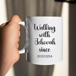 May include: White ceramic mug with the text "Walking with Jehovah since 02.02.2024" in black script. The mug has a curved handle and is held by a hand. The mug is a standard size for coffee or tea.