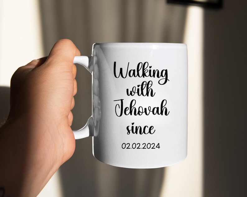 May include: White ceramic mug with the text "Walking with Jehovah since 02.02.2024" in black script. The mug has a curved handle and is held by a hand. The mug is a standard size for coffee or tea.