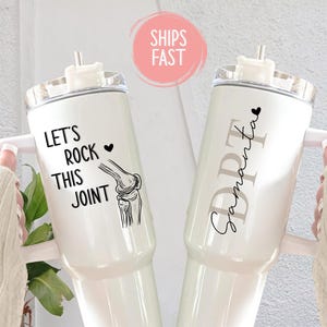 May include: Two white insulated tumblers with handles. One tumbler has the text "Let's Rock This Joint" with a knee joint illustration. The other tumbler has the text "DPT Samantha". Both tumblers have a white lid and a straw.