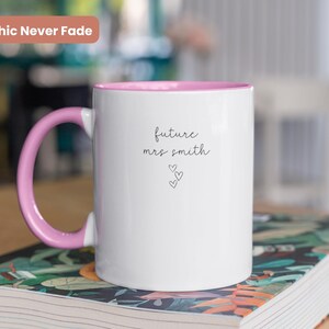 Pu&ograve; includere: Tazza in ceramica bianca con bordo e manico rosa. La tazza ha il testo "future mrs smith" scritto su di essa in corsivo nero con tre piccoli cuori sotto il testo.